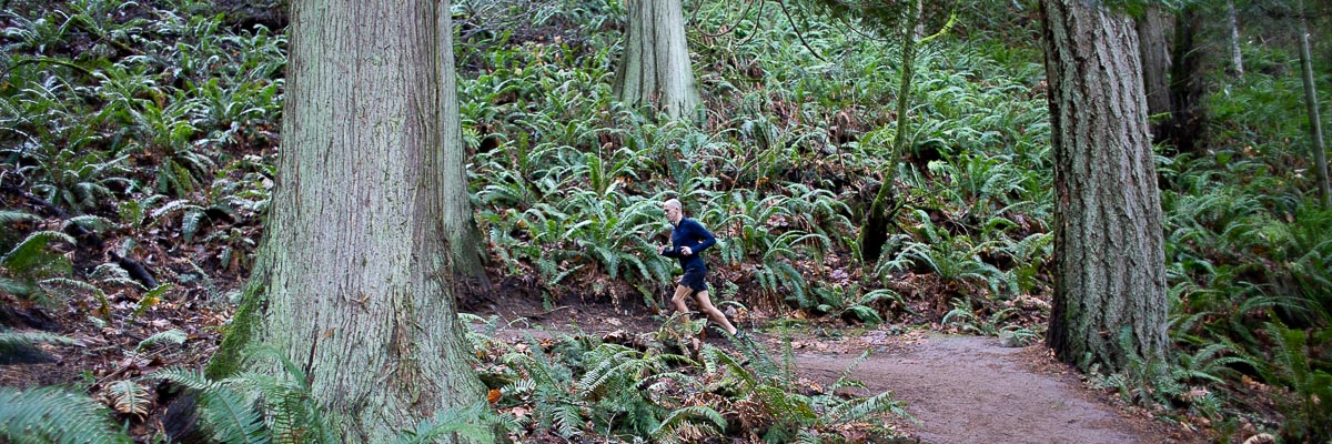 Mac jogging up a hiking trail passing old growth trees.